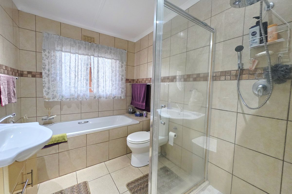 A functional bathroom featuring a built-in bathtub, a separate glass-enclosed shower with rainfall fixture, and neutral ceramic tiling throughout.