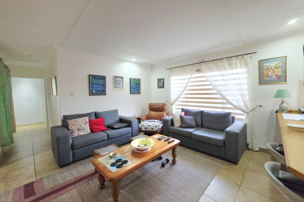 A comfortable living room featuring tiled flooring, neutral walls, and large windows with blinds, providing a bright and functional space for relaxation.