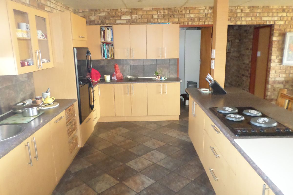 Spacious kitchen featuring light wood cabinetry, dark countertops, an integrated oven and hob, tiled flooring, and rustic exposed brick wall accents.
