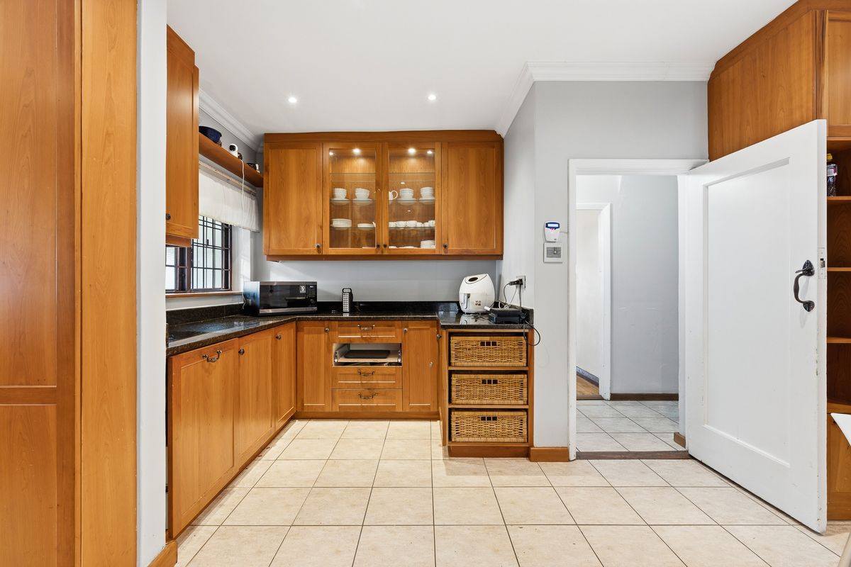 A functional kitchen featuring warm wooden cabinetry, granite countertops, glass-fronted display units, and durable ceramic floor tiles.