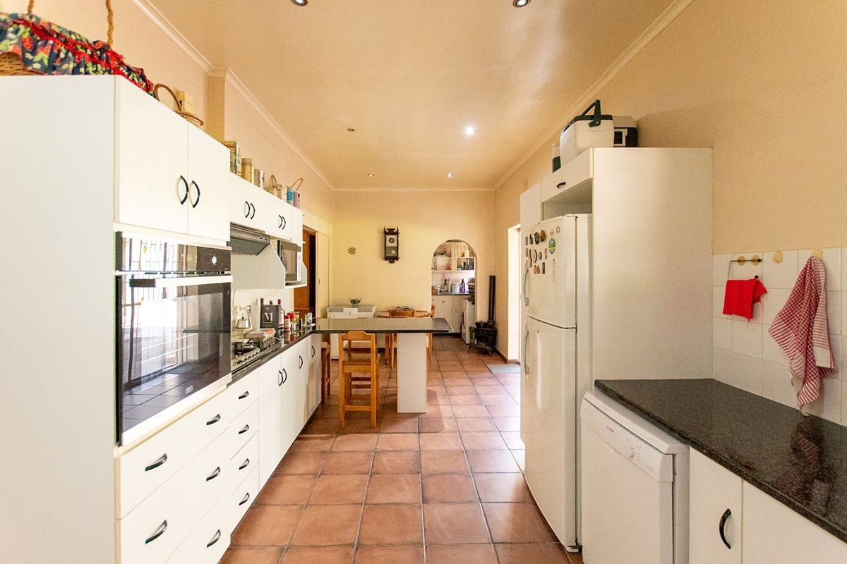 A functional kitchen featuring white cabinetry, built-in oven, hob, and tiled flooring, leading into an adjacent dining area.
