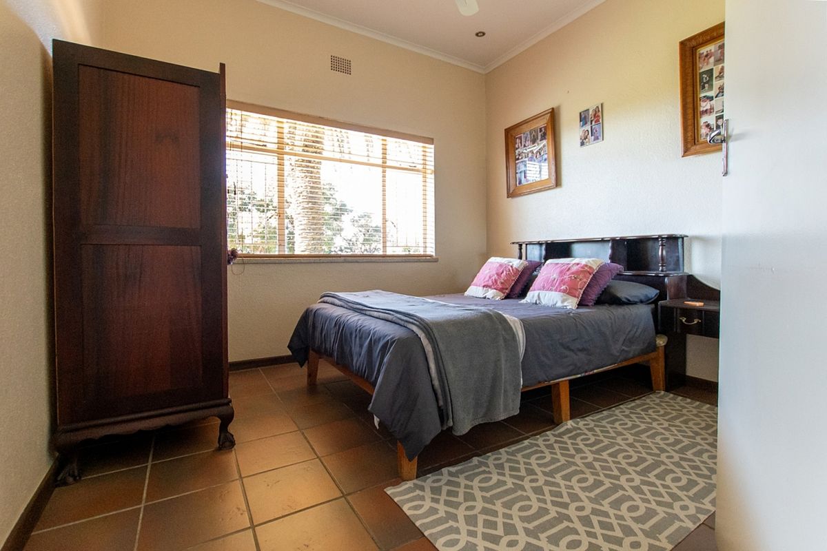 A well-lit bedroom featuring tiled flooring, a large window with blinds, and neutral wall finishes.