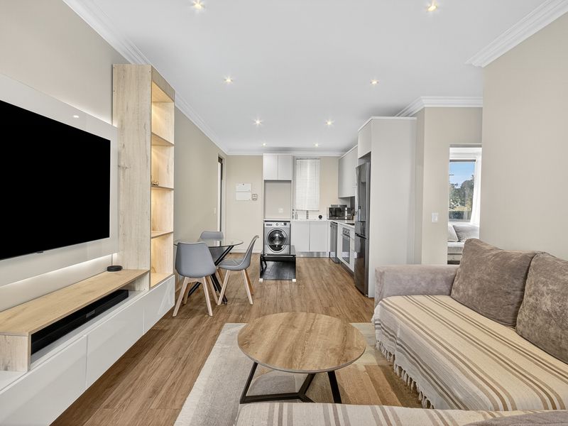 Modern open-plan living area featuring a sleek kitchen, integrated cabinetry, recessed lighting, and durable laminate flooring in a well-maintained apartment setting.