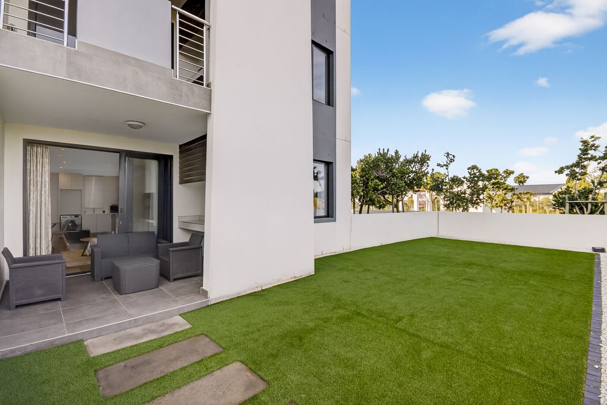 A modern ground floor apartment featuring a covered patio with a built-in braai and a private artificial lawn garden area.