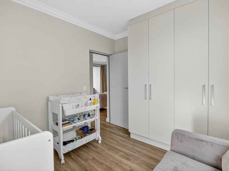 A well-maintained bedroom featuring neutral walls, modern laminate flooring, and ample built-in cupboard storage.