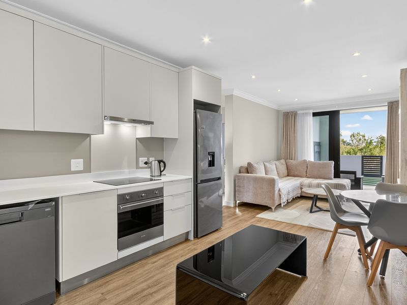 Modern open-plan kitchen and living area featuring sleek cabinetry, integrated appliances, laminate flooring, and direct access to a private balcony.