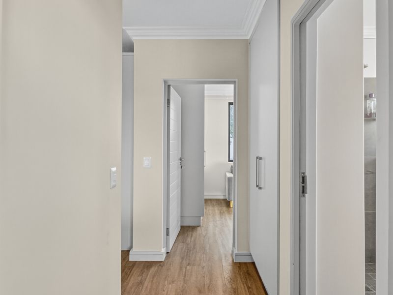A clean, neutral hallway featuring modern laminate flooring, built-in storage cupboards, and classic cornicing, providing seamless access to adjacent living areas and bathroom.