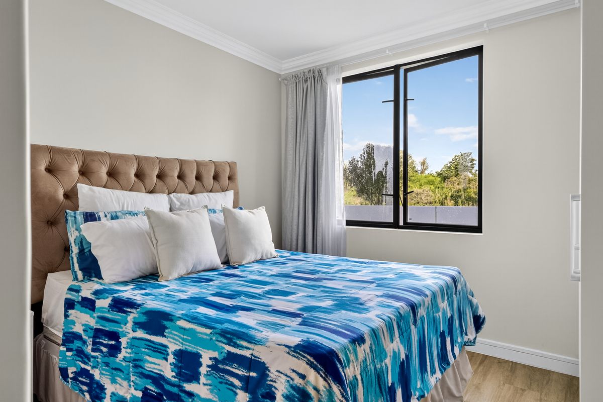 A bright and well-maintained bedroom featuring modern black-framed windows, crown molding, and durable laminate flooring with a pleasant outdoor view.