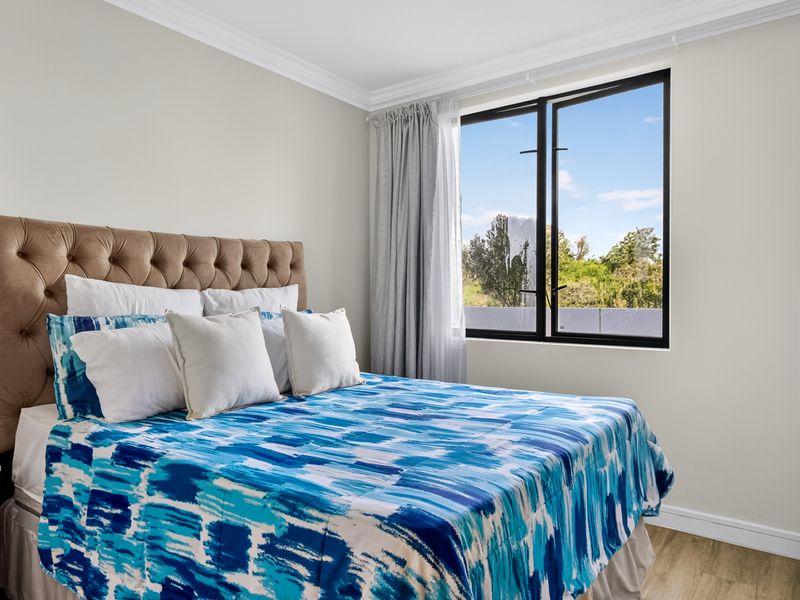 A bright and well-maintained bedroom featuring modern black-framed windows, crown molding, and durable laminate flooring with a pleasant outdoor view.