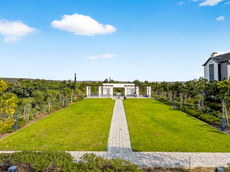 A well-maintained communal garden area featuring a central paved walkway leading to a pergola structure, surrounded by manicured lawns and established landscaping.
