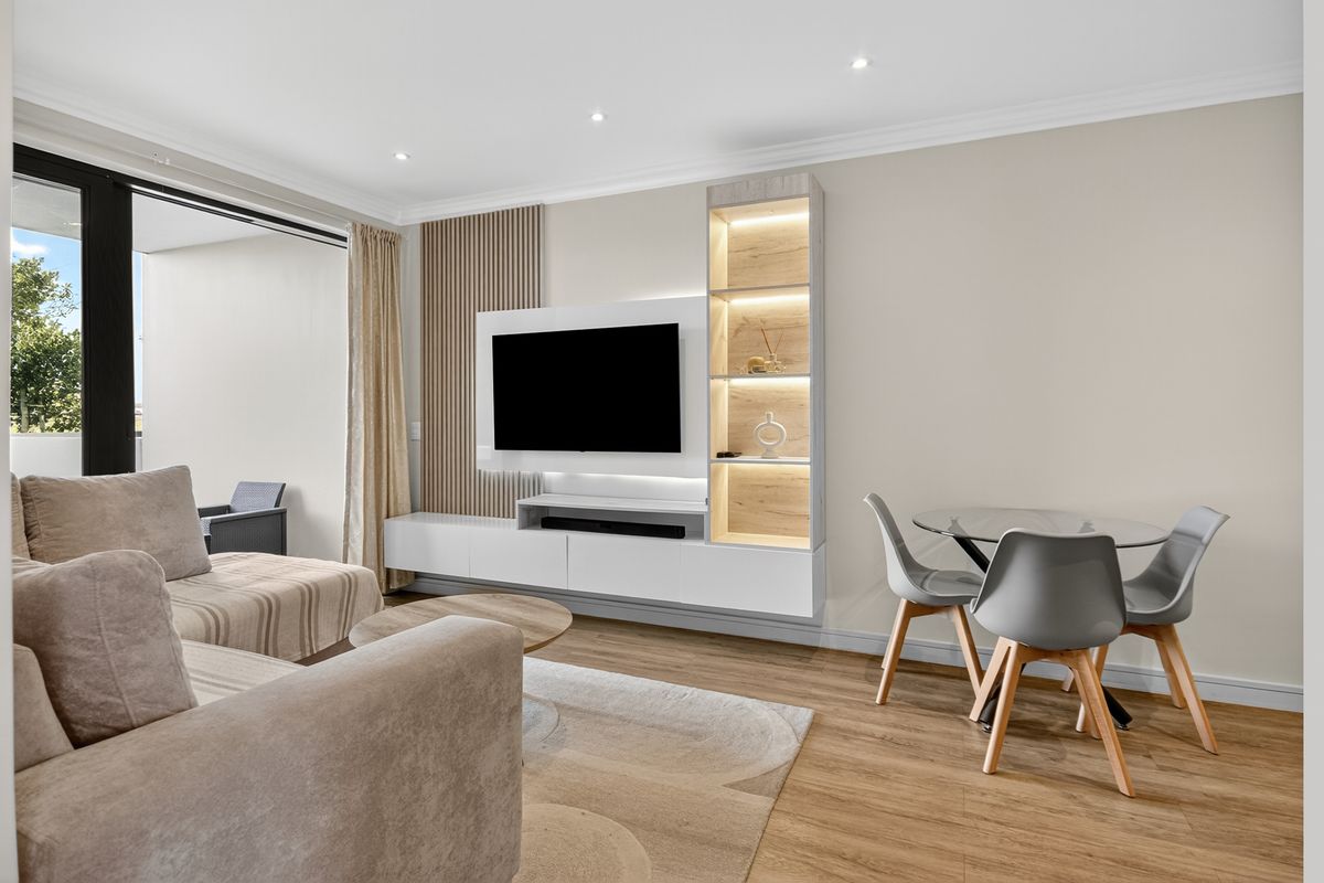 Modern living area featuring a custom built-in media unit with integrated lighting, slatted timber wall accents, and seamless access to the balcony.