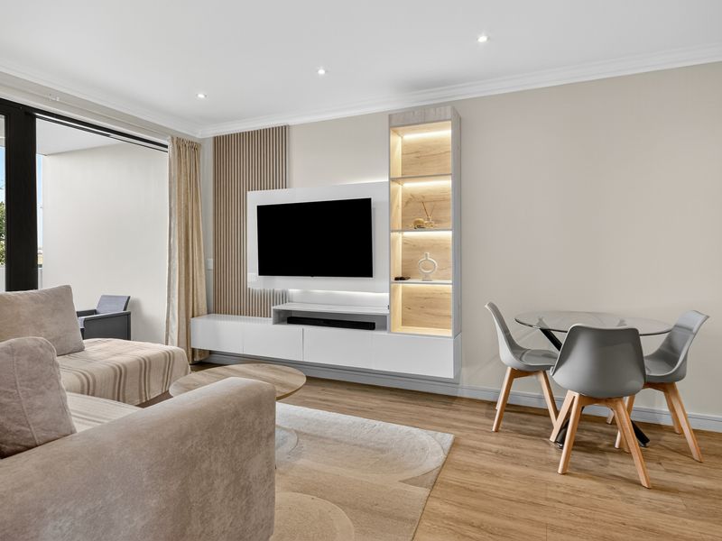 Modern living area featuring a custom built-in media unit with integrated lighting, slatted timber wall accents, and seamless access to the balcony.