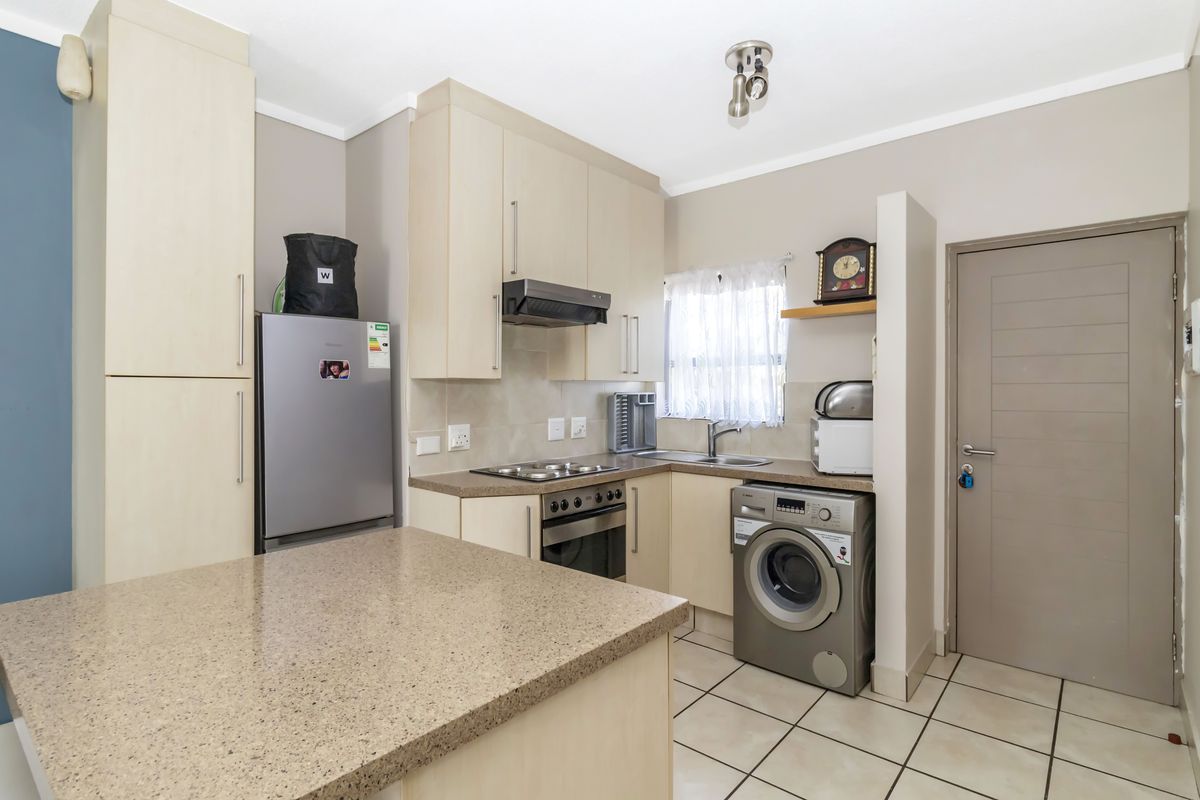 A functional kitchen featuring light wood-finish cabinetry, stone-look countertops, integrated oven and hob, and tiled flooring with space for laundry appliances.