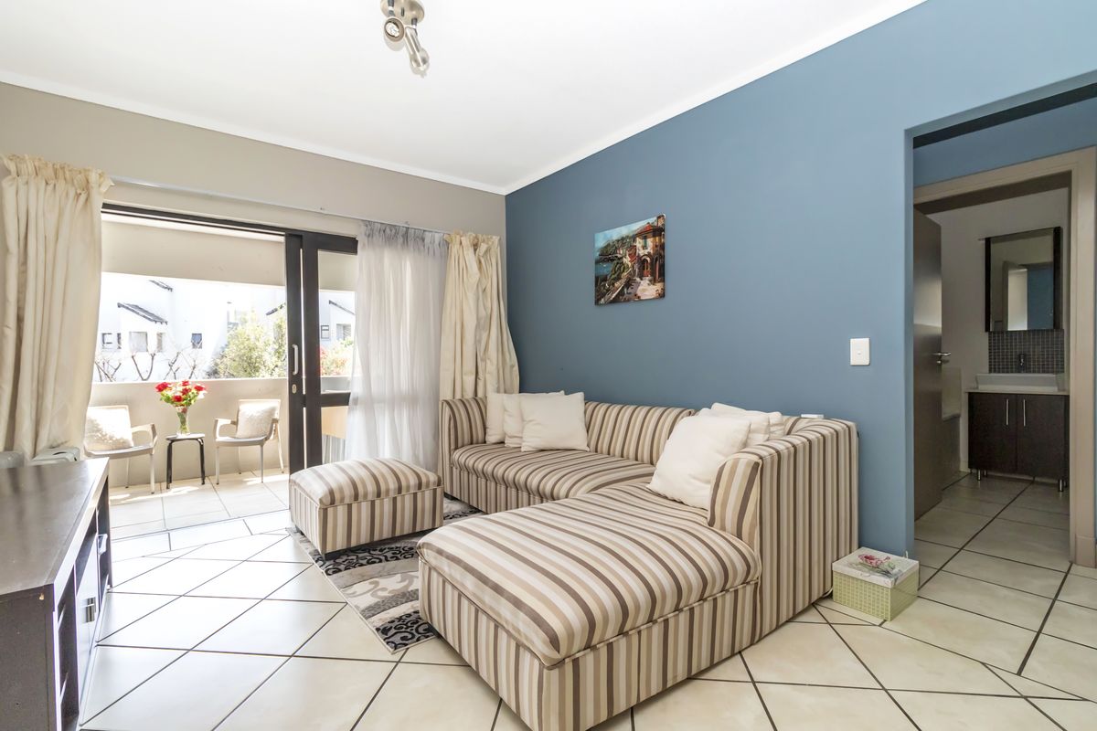 A bright living room featuring tiled floors, a blue accent wall, and a sliding glass door leading to a private balcony.