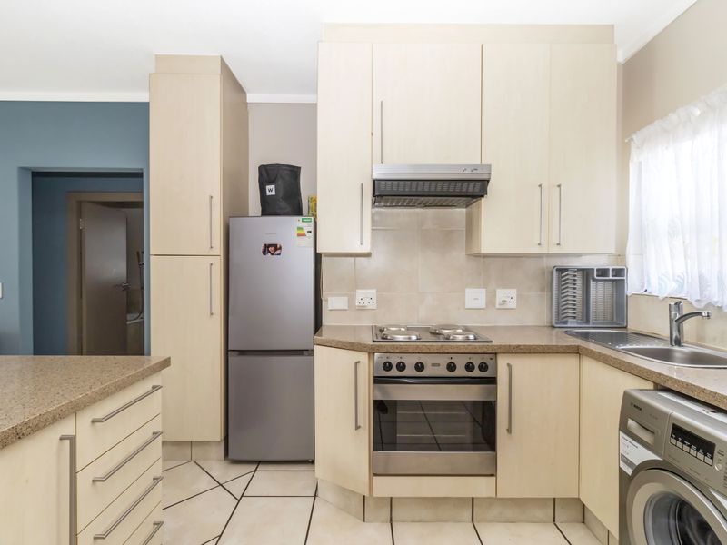 Functional kitchen featuring light wood-finish cabinetry, stone-look countertops, built-in oven with hob, extractor fan, and tiled flooring.