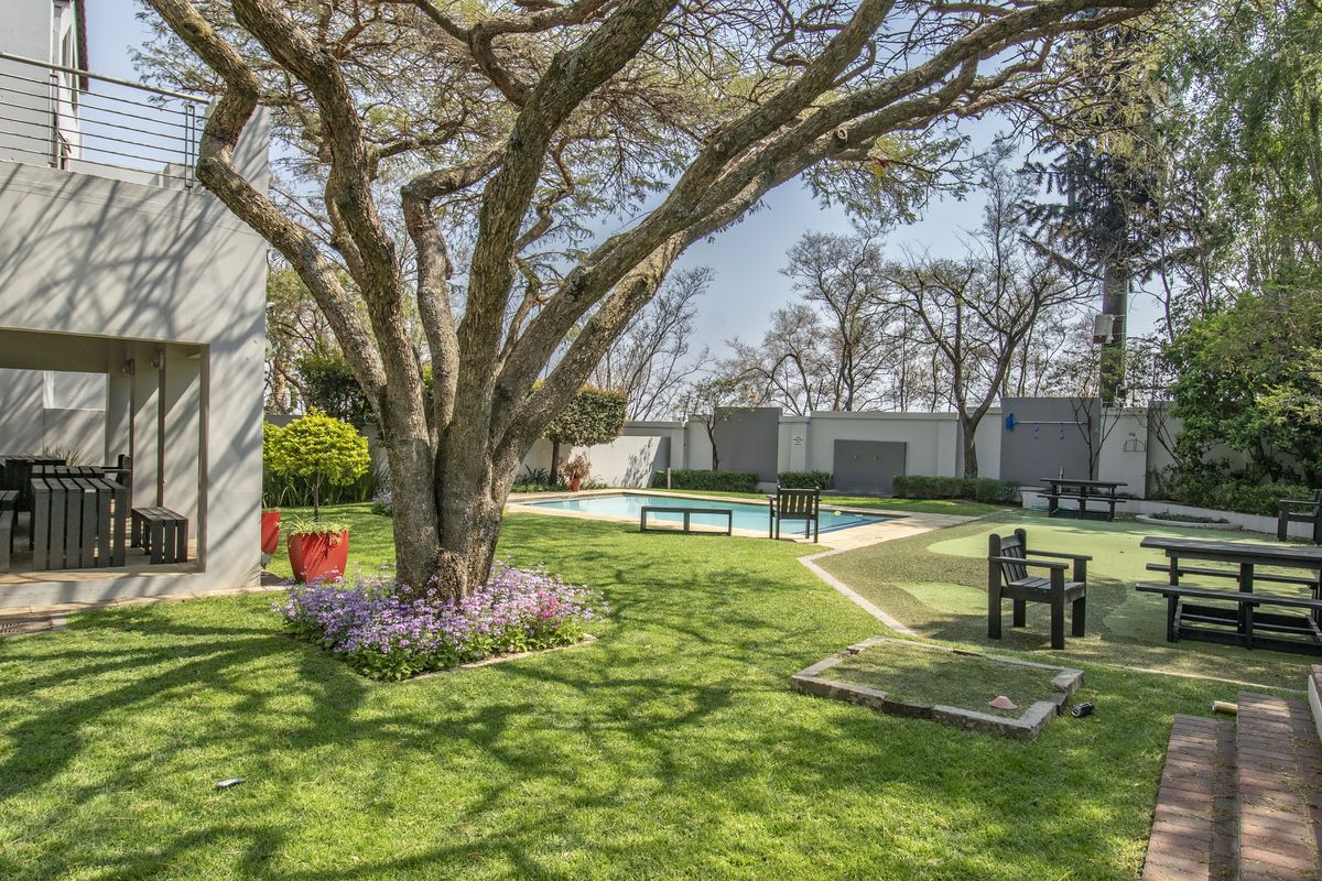 A spacious rear garden featuring a swimming pool, covered patio area, mature tree, and well-maintained lawn with artificial turf sections.