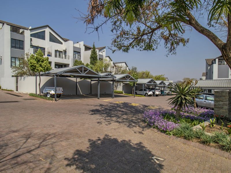 Exterior view of the apartment complex featuring a paved driveway, covered parking bays, and well-maintained landscaped garden areas.