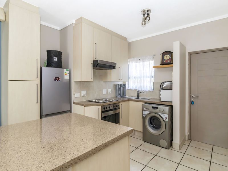 A functional kitchen featuring light wood-finish cabinetry, stone-look countertops, integrated oven and hob, and tiled flooring with space for laundry appliances.