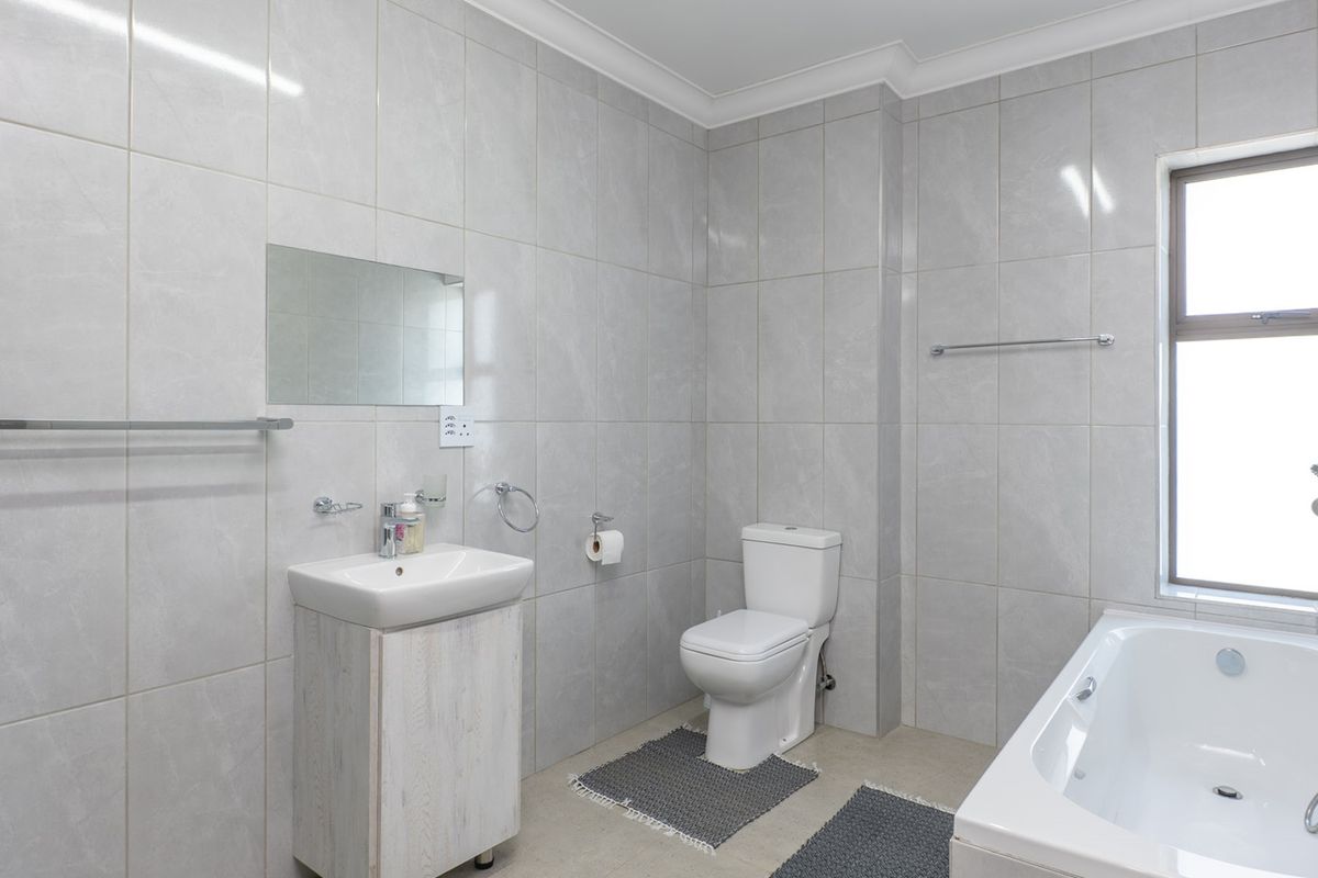 A clean, modern bathroom featuring tiled walls, a vanity cabinet with basin, a toilet, and a bathtub with a window for natural light.