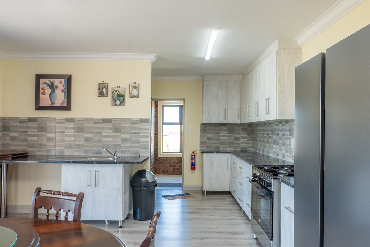 A functional kitchen featuring light wood-grain cabinetry, tiled backsplash, gas stove, and laminate countertops, leading to a rear entrance area.