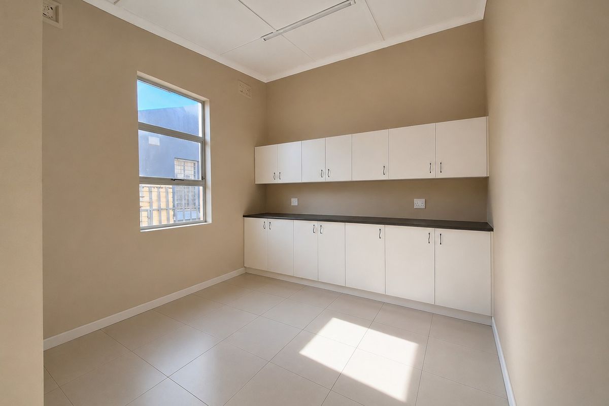 A clean, empty utility room or office space featuring built-in white cabinetry, dark countertops, and tiled flooring.
