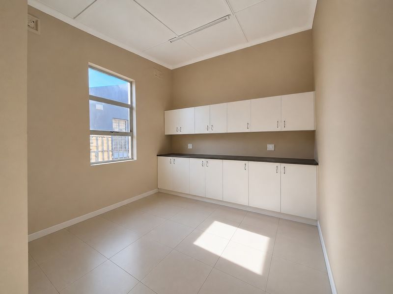 A clean, empty utility room or office space featuring built-in white cabinetry, dark countertops, and tiled flooring.