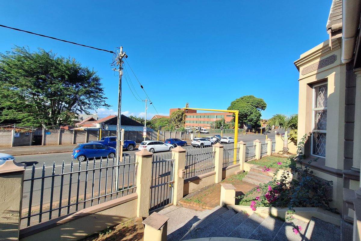 Exterior view of the property boundary featuring a metal security fence, gated entrance, and paved steps leading to the building facade.