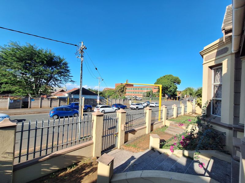 Exterior view of the property boundary featuring a metal security fence, gated entrance, and paved steps leading to the building facade.