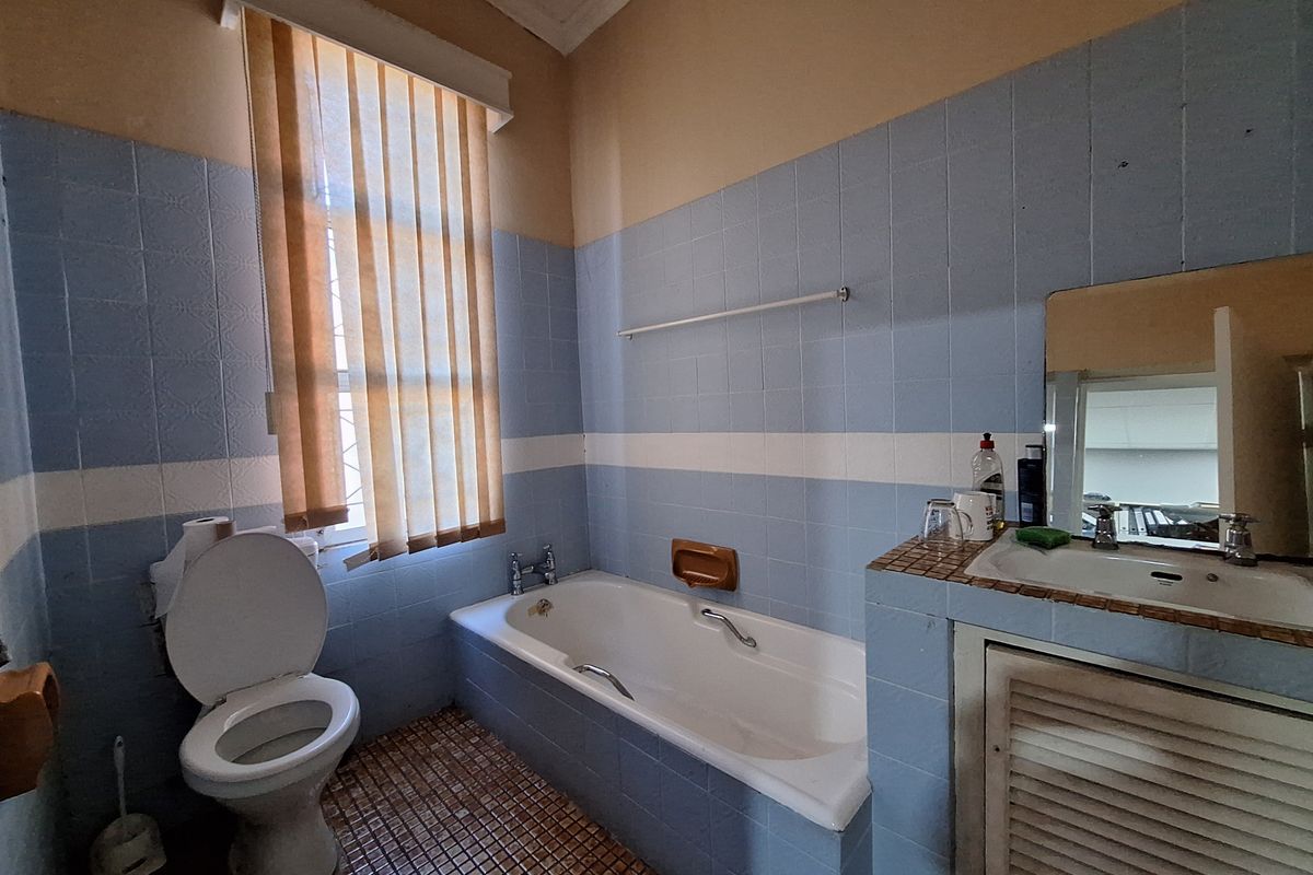 A dated bathroom featuring a built-in bathtub, a vanity basin with storage, and a toilet, finished with blue and white wall tiles.