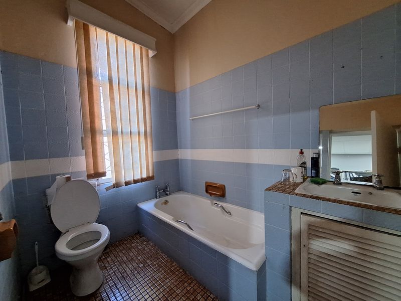 A dated bathroom featuring a built-in bathtub, a vanity basin with storage, and a toilet, finished with blue and white wall tiles.