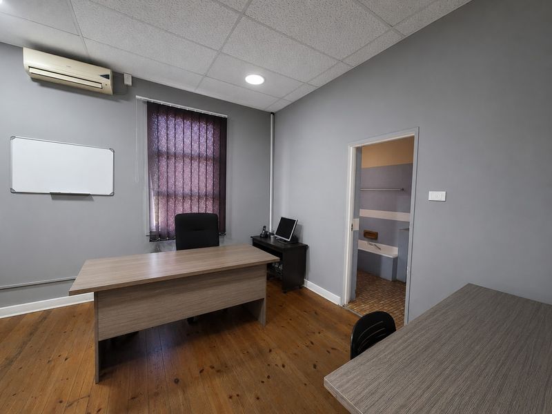 A functional office space featuring timber flooring, a wall-mounted air conditioning unit, and direct access to an adjoining bathroom.