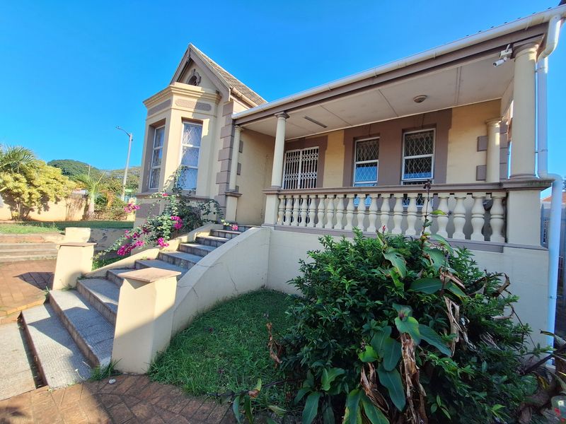 A classic home featuring a covered veranda with balustrades, stone-tiled stairs, and traditional architectural detailing, set within a landscaped garden.
