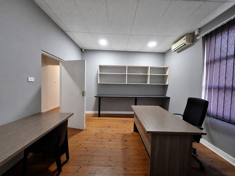 A functional home office featuring timber flooring, built-in wall shelving, a desk area, and a wall-mounted air conditioning unit.