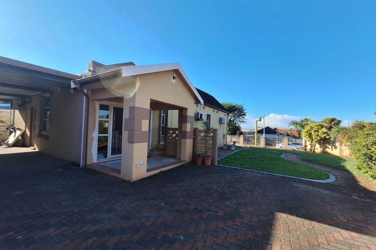 Exterior view of the house featuring a paved driveway, covered entrance porch, and a small landscaped garden area.