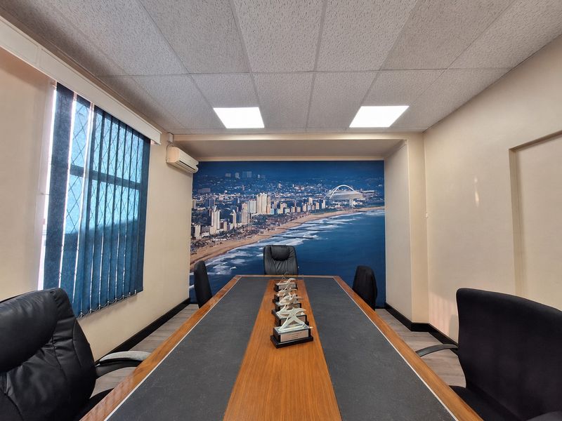A professional office or boardroom space featuring a large feature wall mural, recessed ceiling lighting, and vertical window blinds.