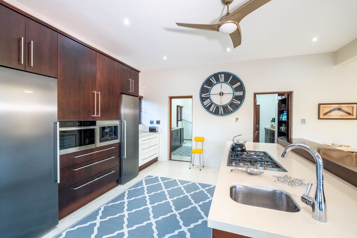 Modern kitchen featuring dark wood cabinetry, stone countertops, a central island with a gas hob, and integrated appliances.