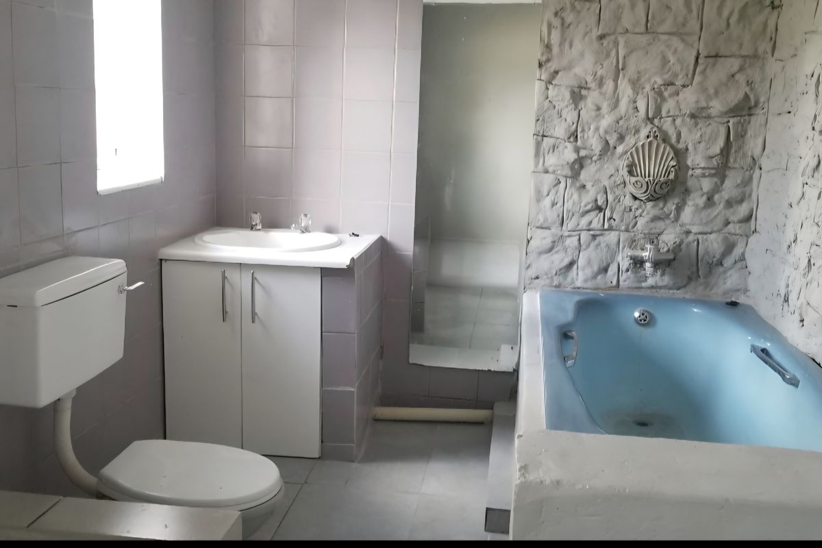 A dated bathroom featuring a blue bathtub, a vanity cabinet with a basin, and a toilet, finished with light-colored wall tiles and stone-effect accents.