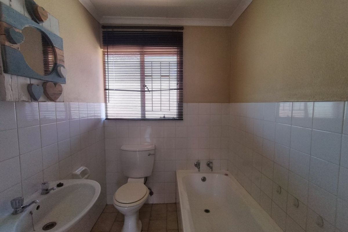 A functional bathroom featuring a standard bathtub, pedestal basin, and toilet, finished with half-height wall tiling and neutral paint.