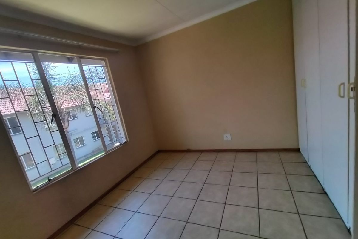 A vacant bedroom featuring tiled flooring, built-in cupboards, and security bars on the window.