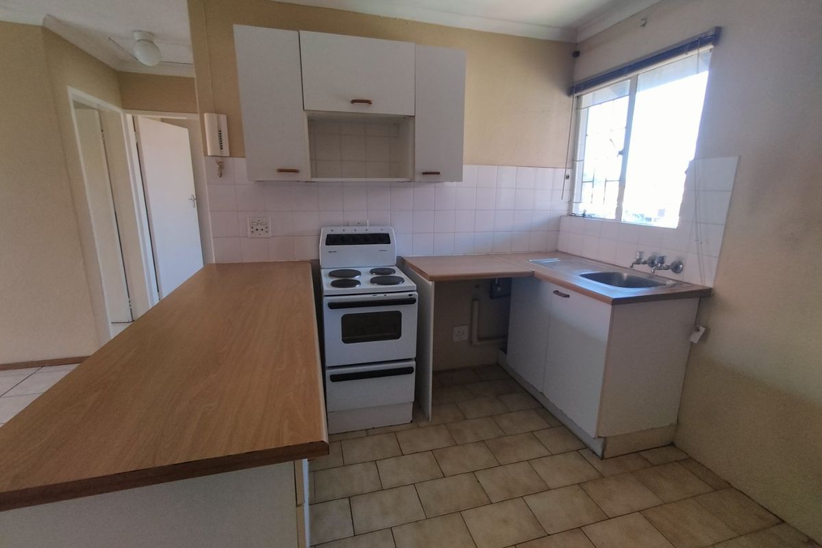 A functional kitchen featuring laminate countertops, a freestanding stove, tiled splashbacks, and basic cabinetry, offering potential for modernization.