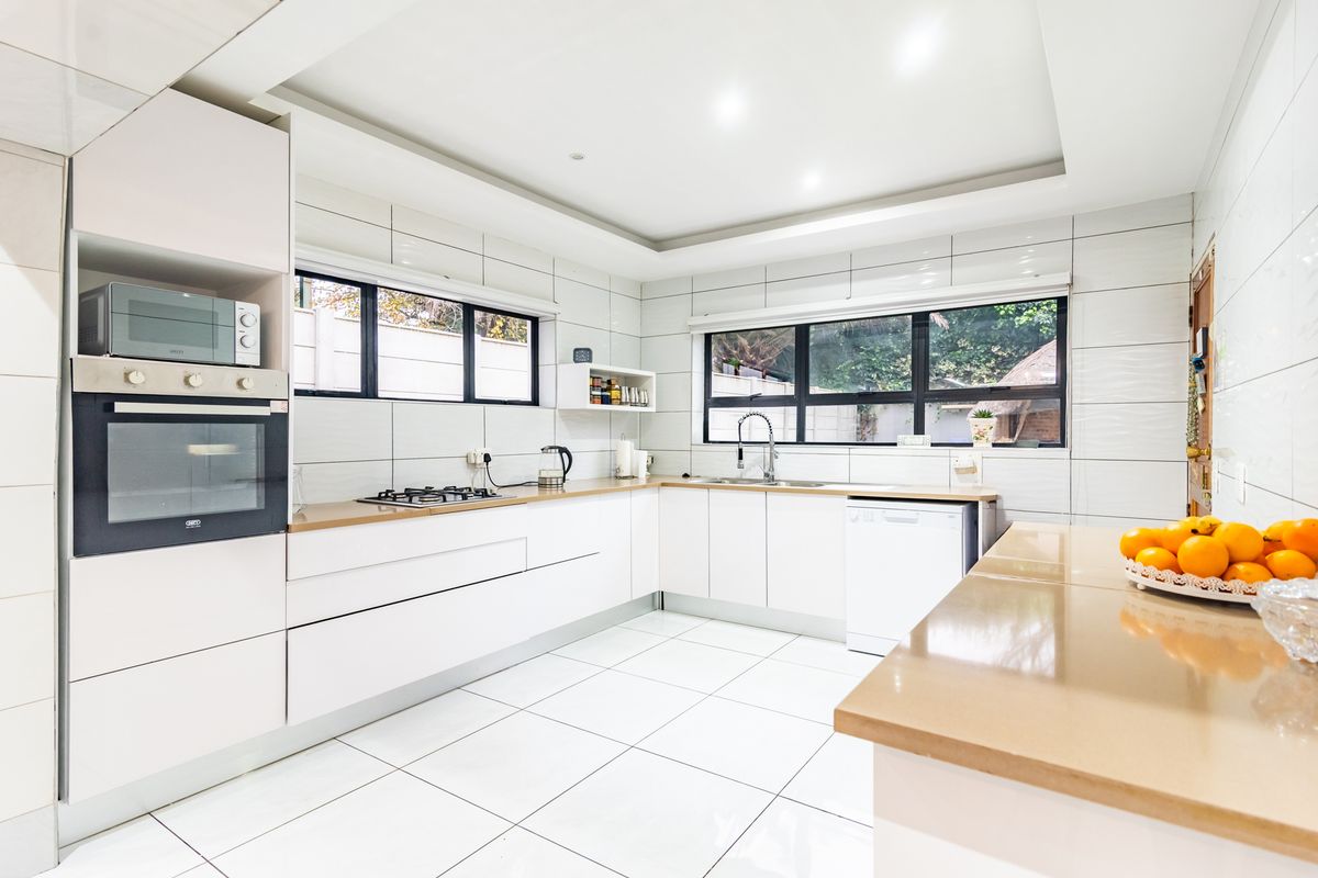 Modern kitchen featuring white cabinetry, stone countertops, built-in oven, gas hob, and large windows providing ample natural light.