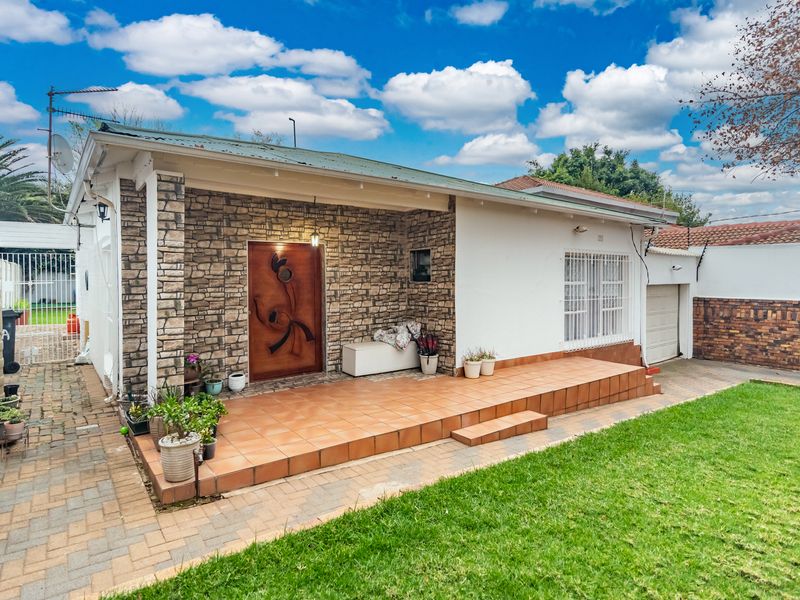 Front elevation of a single-story house featuring a tiled patio, stone cladding accents, a paved driveway, and a secure entrance.