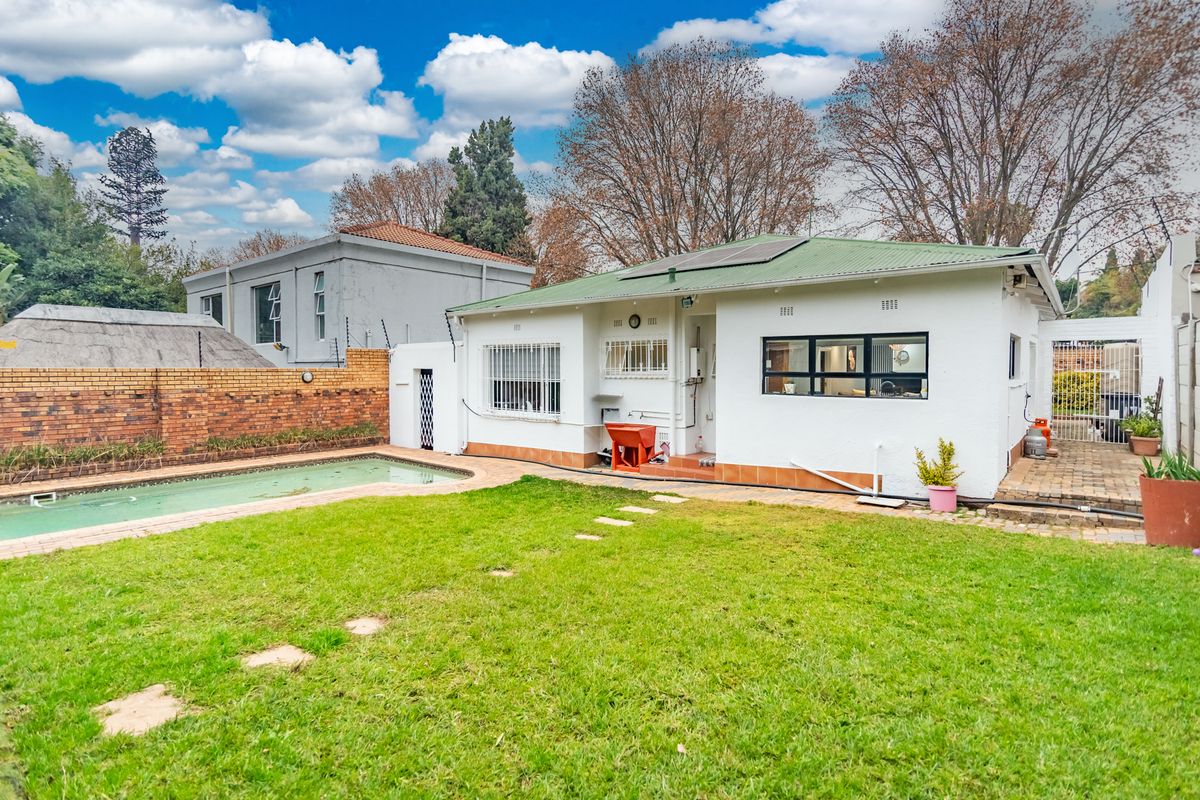 Rear view of the property featuring a swimming pool, a lawned garden, and a white-painted exterior with a green metal roof.