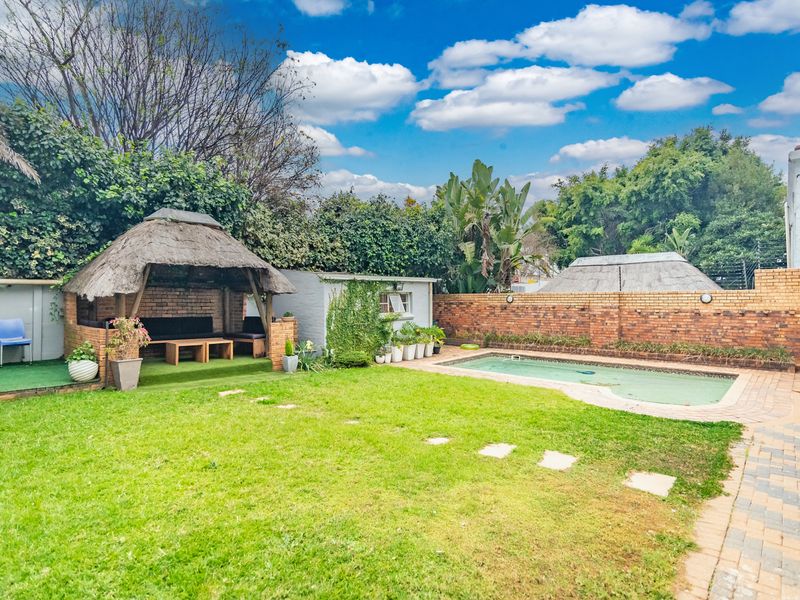 Outdoor entertainment area featuring a swimming pool, a thatched lapa, and a private garden with brick boundary walls.