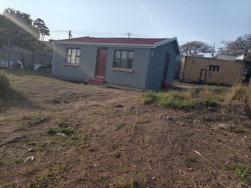 A detached single-story house featuring a tiled roof and grey exterior walls, situated on an unlandscaped plot of land.