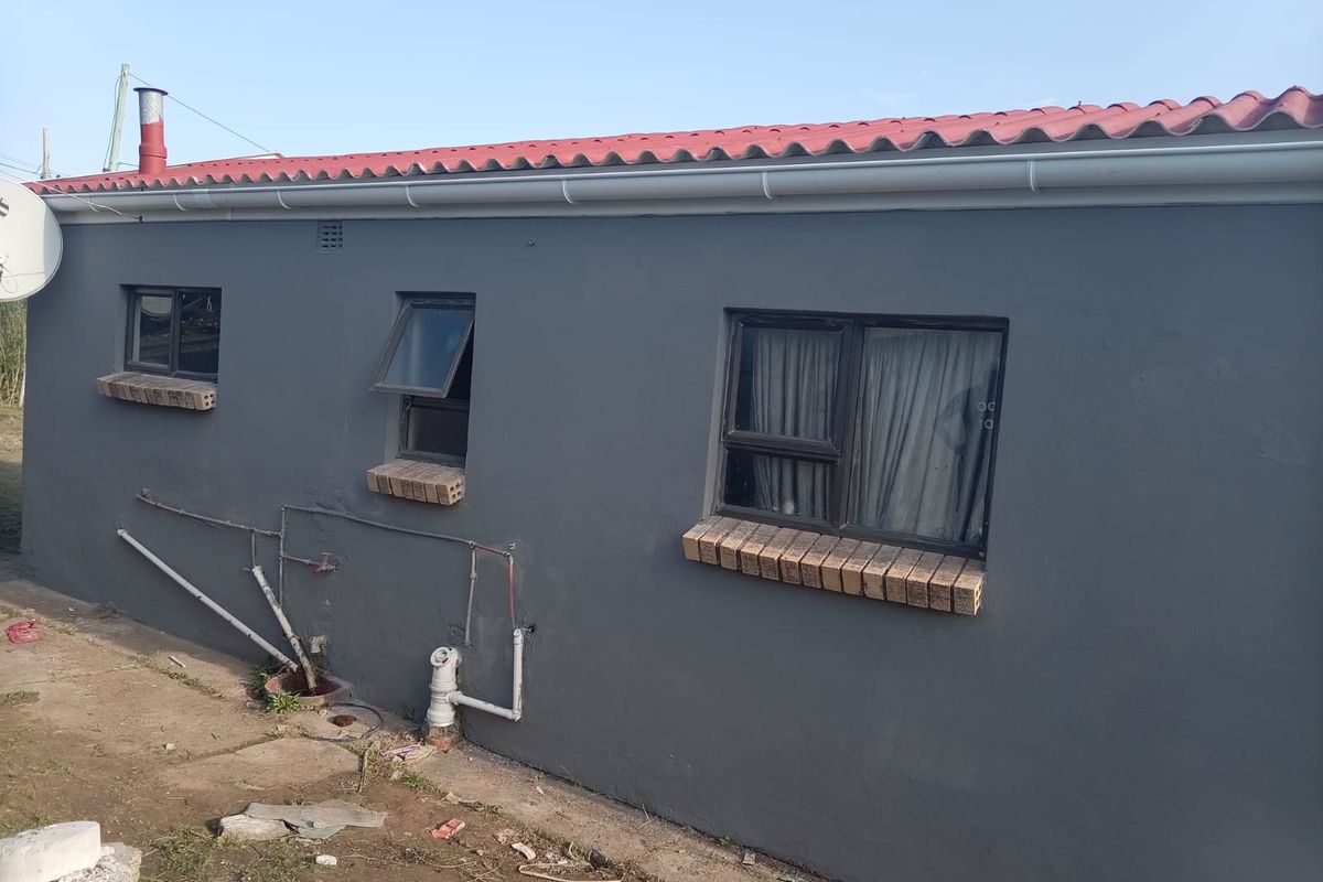 Rear exterior view of the house featuring a painted grey facade, corrugated metal roof, and external plumbing fixtures.