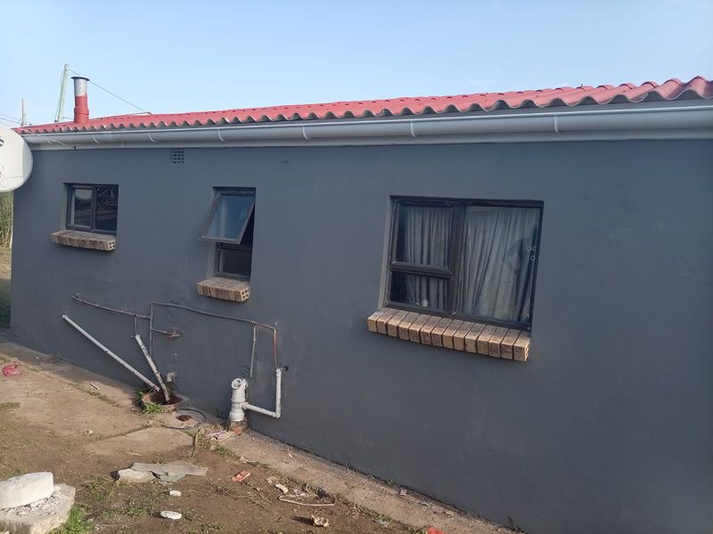 Rear exterior view of the house featuring a painted grey facade, corrugated metal roof, and external plumbing fixtures.