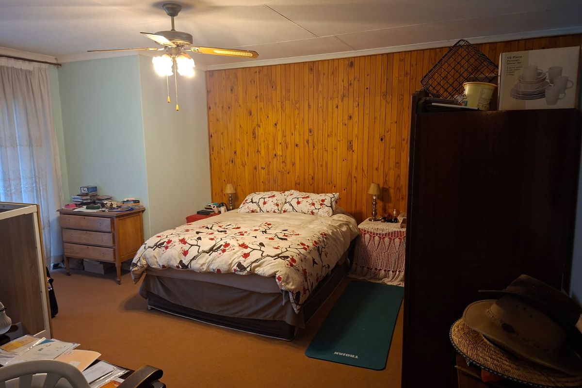 A bedroom featuring wood-paneled accent wall, ceiling fan, and carpeted flooring.