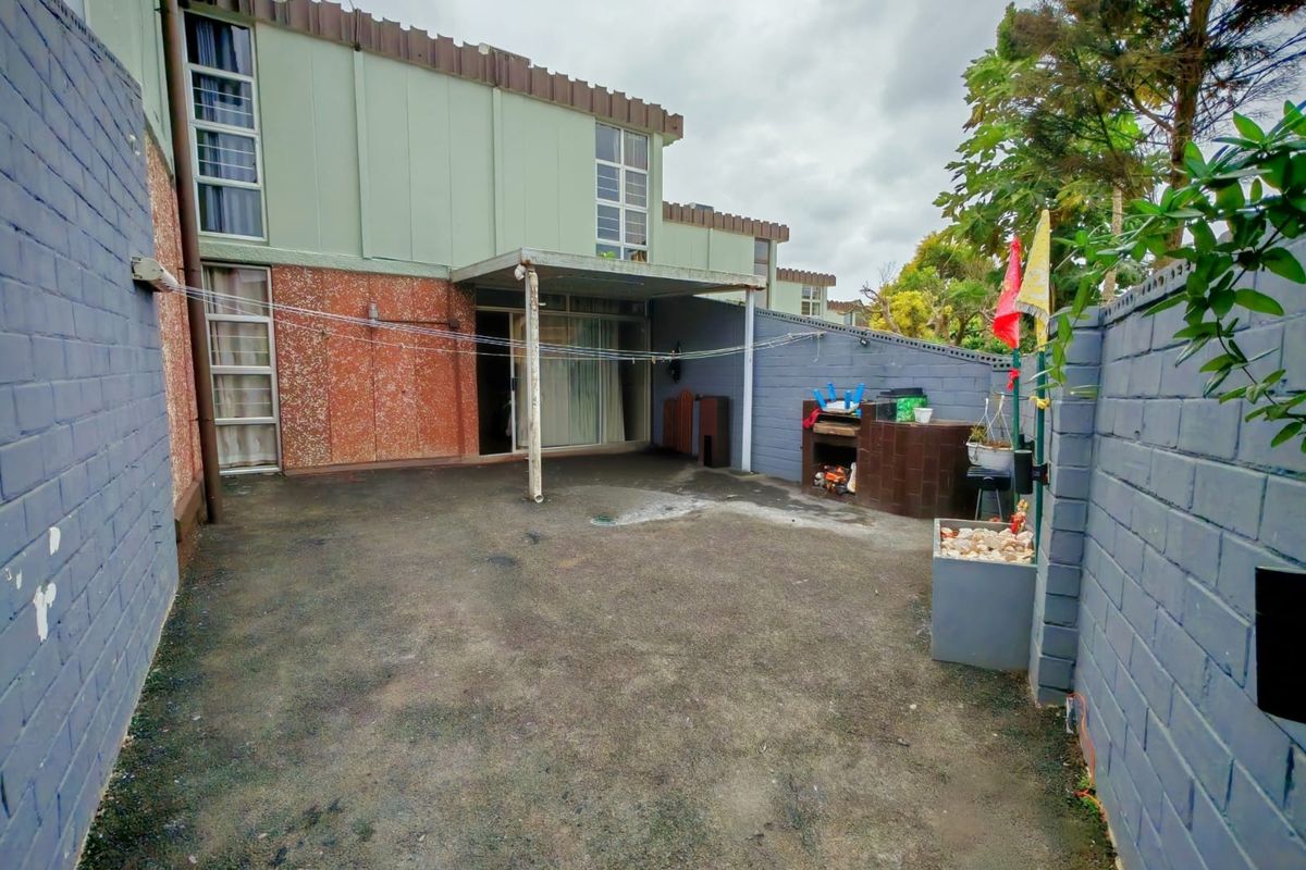A private rear courtyard featuring a covered patio area, built-in brick braai, and enclosed by painted masonry boundary walls.