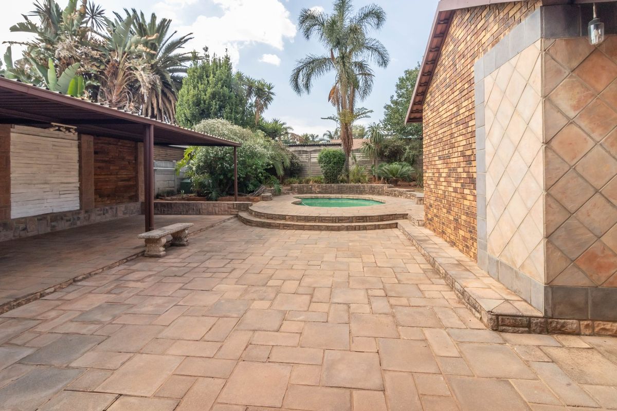 A spacious rear patio area featuring paved flooring, a covered entertainment section, and a raised circular plunge pool set within a landscaped garden.